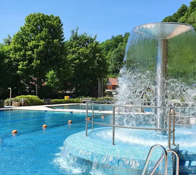 Erfrischender Brunnen im Naturbad Elbingerode, umgeben von grünen Bäumen und blauem Wasser.
