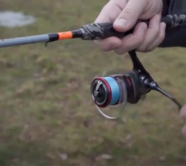 Daiwa Fuego Camo Spin Test: Eine Hand hält eine Angelrute mit Camo-Griff und einer Rolle mit blauer Schnur.
