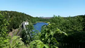 Idyllische Badeseen in Sachsen-Anhalt: Ein Stausee mit Damm und kleinem Haus, umgeben von grünen Wäldern unter blauem Himmel.
