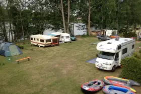 Campingplatz am sonnensee flachslanden mit Wohnmobilen, Wohnwagen, Zelt und Schlauchbooten am Ufer.