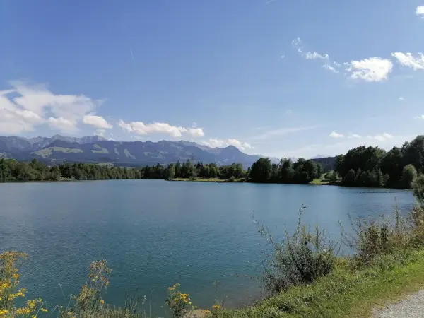 Blauer Himmel über dem Sonthofener See, umgeben von grünen Bäumen und majestätischen Bergen.