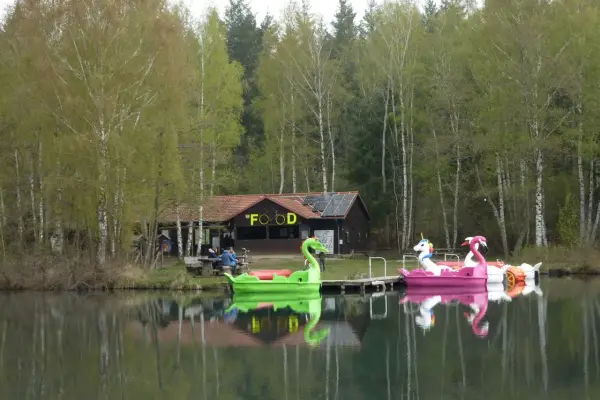 Bunte Tretboote in Form von Schwänen und Einhörnern liegen am Ufer des Bruchsee Duingen. Ein Gebäude mit der Aufschrift "FOOD" und Solaranlagen steht im Hintergrund.
